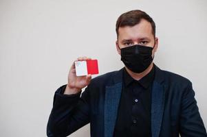 European man wear black formal and protect face mask, hold Malta flag card isolated on white background. Europe coronavirus Covid country concept. photo