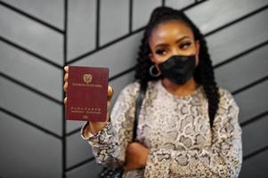 African american woman wearing black face mask show Colombia passport in hand. Coronavirus in America country, border closure and quarantine, virus outbreak concept. photo