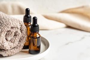 set of different bottles with beauty serum, hyaluronic acid and vitamins on wooden tray with towel. Home spa concept photo