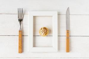 concepto de alimentación y dieta saludable. pequeño postre en un marco de fotos servido con tenedor y cuchillo en una mesa blanca