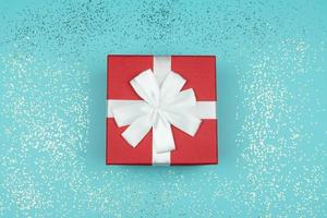 vista superior de la caja de regalo roja sobre fondo azul con confeti. tarjeta de felicitación navideña festiva. foto