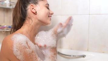 mujer joven en baño de burbujas se ríe y acaricia burbujas en el cuerpo y la cara video