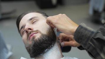 barbeiro usa navalha para raspar o pescoço e o rosto do homem para moldar o cabelo facial video