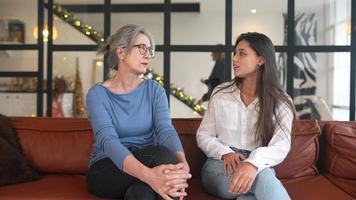 Older woman and young woman sit and talk to each other in office interior with holiday lights in the background video