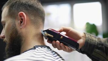 Barber trims back of head hair and neck of male client with comb and clippers
