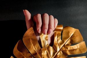 woman hand with ethnic manicure holding gold leaf of monstera. Black background photo