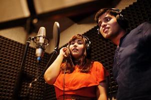 Young asian duet singers with microphone recording song in record music studio. photo