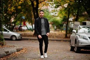 Portrait of stylish arab beard man wear grey turtleneck and black jaket. Arabian model guy on a background of autumn leaves. photo