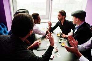 Arm competition. Group of handsome retro well-dressed man gangsters spend time at club, sitting and drinking whiskey. Multiethnic male bachelor mafia party in restaurant. photo