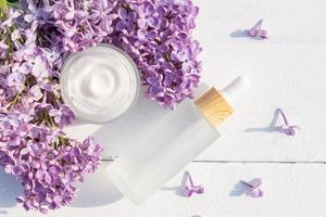 Concept skin care. A set of cosmetic products, creams and serum. Frosted glass bottles on white background with lilac flowers. Rejuvenation and moisturizing. Flat lay. photo