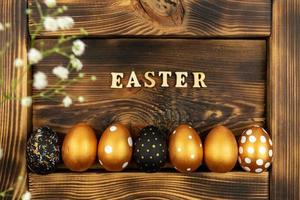 Easter festive background. Top view of easter eggs colored with golden paint and inscription in English Easter. Wooden letters on dark wood background. Various dotted design photo