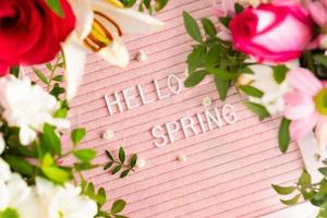 Text Hello Spring on pink letter board and frame of blooming flowers. Concept Springtime mood and happiness. photo