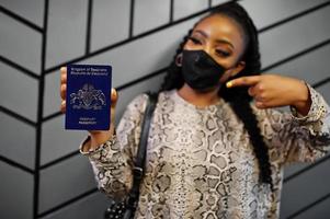 African woman wearing black face mask show Eswatini passport in hand. Coronavirus in Africa country, border closure and quarantine, virus outbreak concept. photo