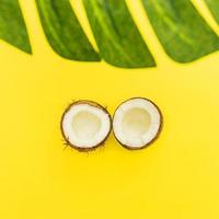 Bright tropical background with broken cocnut and monstera leaf, minimal flat lay photo