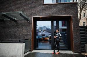 Fashionable beautiful african american woman posing in black leather jacket and pants at street. photo