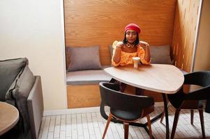 Elegant afro american woman in red french beret, big gold neck chain polka dot blouse and leather pants pose indoor. photo