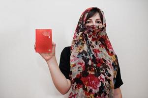 Young arabian muslim woman in hijab clothes hold Swiss Confederation passport on white wall background, studio portrait. photo