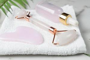 Pink roller face massager Guasha Scraper. Jade stone face massager for face and body with dropper bottle of beauty serum. trendy fashion concept. Anti-aging, lifting and toning care at home. photo