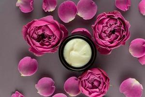 Face care cream in a jar on a brown background with beautiful roses. anti-aging cream. Cream for skin care. Beauty treatment concept photo