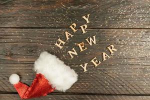 festive greeting card for new year with red santa hat and wooden text scettered out of it on a table. copy psace for text. Holiday concept photo