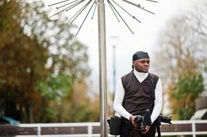 Young professional african american videographer holding professional camera with pro equipment. Afro cameraman wearing black duraq making a videos. photo