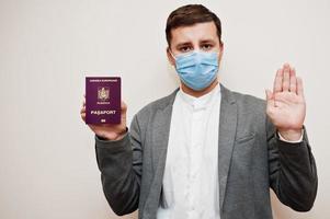 European man in formal wear and face mask, show AAA passport with stop sign hand. Coronavirus lockdown in Europe country concept. photo