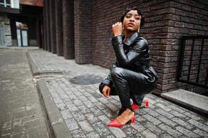 Fashionable beautiful african american woman posing in black leather jacket and pants at street. photo