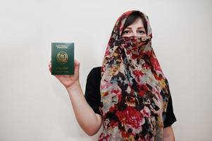 joven musulmana árabe vestida con hijab tiene pasaporte de la república islámica de pakistán sobre fondo de pared blanca, retrato de estudio. foto