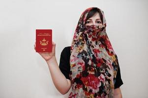 joven musulmana árabe vestida con hiyab sostiene la nación de brunei, la morada del pasaporte de paz sobre fondo de pared blanca, retrato de estudio. foto