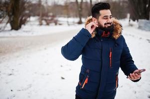 Beard indian man wear jacket in cold winter day. He speak mobile phone by wireless headphones. photo