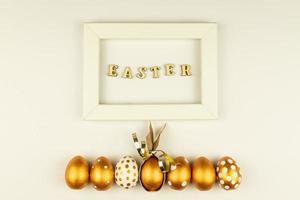 Easter festive decoration. Top view of easter eggs colored with golden paint and empty mock-up photo frame. Various dotted designs. White background.