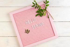 Text Hello Spring on the pink letter board with green branches on wooden background, minimalism style composition, copy space for your text. photo