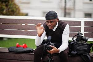 Young professional african american videographer holding professional camera with pro equipment. Afro cameraman wearing black duraq making a videos. photo