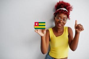 mujer africana con cabello afro, use camiseta amarilla y anteojos, sostenga la bandera de togo aislada en fondo blanco, muestre el pulgar hacia arriba. foto