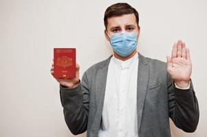 European man in formal wear and face mask, show Latvia passport with stop sign hand. Coronavirus lockdown in Europe country concept. photo