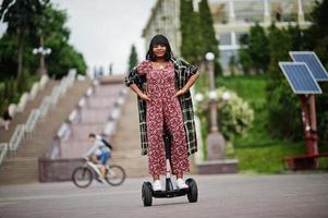 hermosa mujer afroamericana usando segway o hoverboard. chica negra en scooter eléctrico autoequilibrado de doble rueda. foto