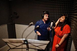Young asian duet singers with microphone recording song in record music studio. photo