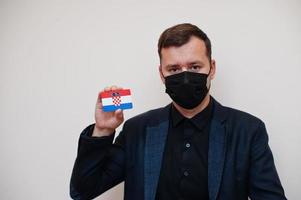 European man wear black formal and protect face mask, hold Croatia flag card isolated on white background. Europe coronavirus Covid country concept. photo