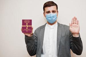 European man in formal wear and face mask, show Svalbard passport with stop sign hand. Coronavirus lockdown in Europe country concept. photo