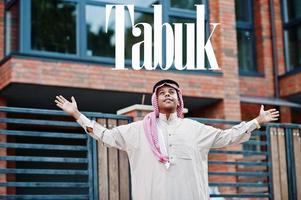 Tabuk - biggest city of Saudi Arabia. Middle Eastern saudi arabian man posed on street against modern building up his hands in the air. photo