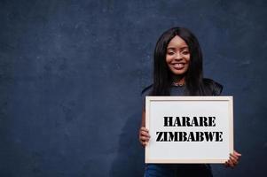 mujer africana sostiene una pizarra blanca con la inscripción harare zimbabwe. concepto de ciudad más poblada de África. foto