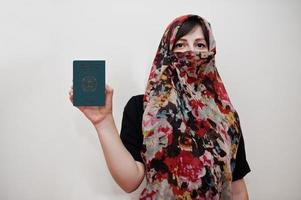 joven musulmana árabe vestida con hijab tiene pasaporte de la república islámica de afganistán sobre fondo de pared blanca, retrato de estudio. foto