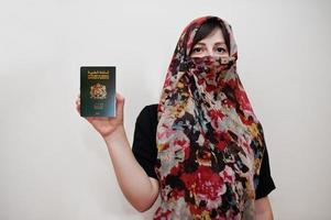 joven musulmana árabe vestida con hiyab tiene pasaporte del reino de marruecos sobre fondo de pared blanca, retrato de estudio. foto
