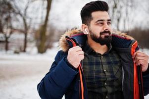 Beard indian man wear jacket in cold winter day. Mobile earphones in ears. photo