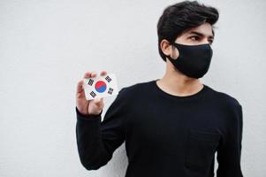 Asian man wear all black with face mask hold South Korea Korea flag in hand isolated on white background. Coronavirus country concept. photo