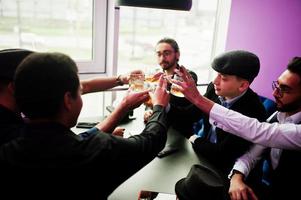 Group of handsome retro well-dressed man gangsters spend time at club, sitting and drinking whiskey. Multiethnic male bachelor mafia party in restaurant. photo