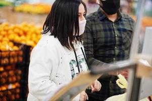 Asian couple wear in protective face mask shopping together in supermarket during pandemic. Weigh the goods. photo