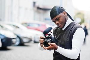 Young professional african american videographer holding professional camera with pro equipment. Afro cameraman wearing black duraq making a videos. photo