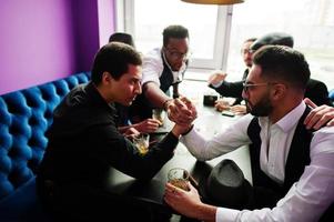 Arm competition. Group of handsome retro well-dressed man gangsters spend time at club, sitting and drinking whiskey. Multiethnic male bachelor mafia party in restaurant. photo