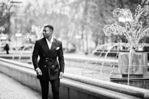 Portrait of young and handsome african american businessman in suit walking on cemter of city with garlands. photo